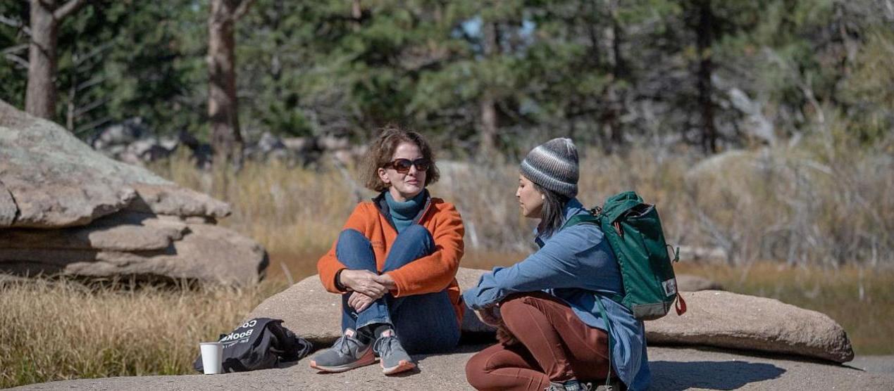 two people sitting and talking on a large rock